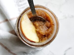 Homemade date-sweetened applesauce in a mason jar served with an apple slice and a spoon.