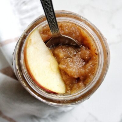 Homemade date-sweetened applesauce in a mason jar served with an apple slice and a spoon.