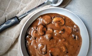 Sliced mushroom gravy in a gray bowl with a sauce serving spoon