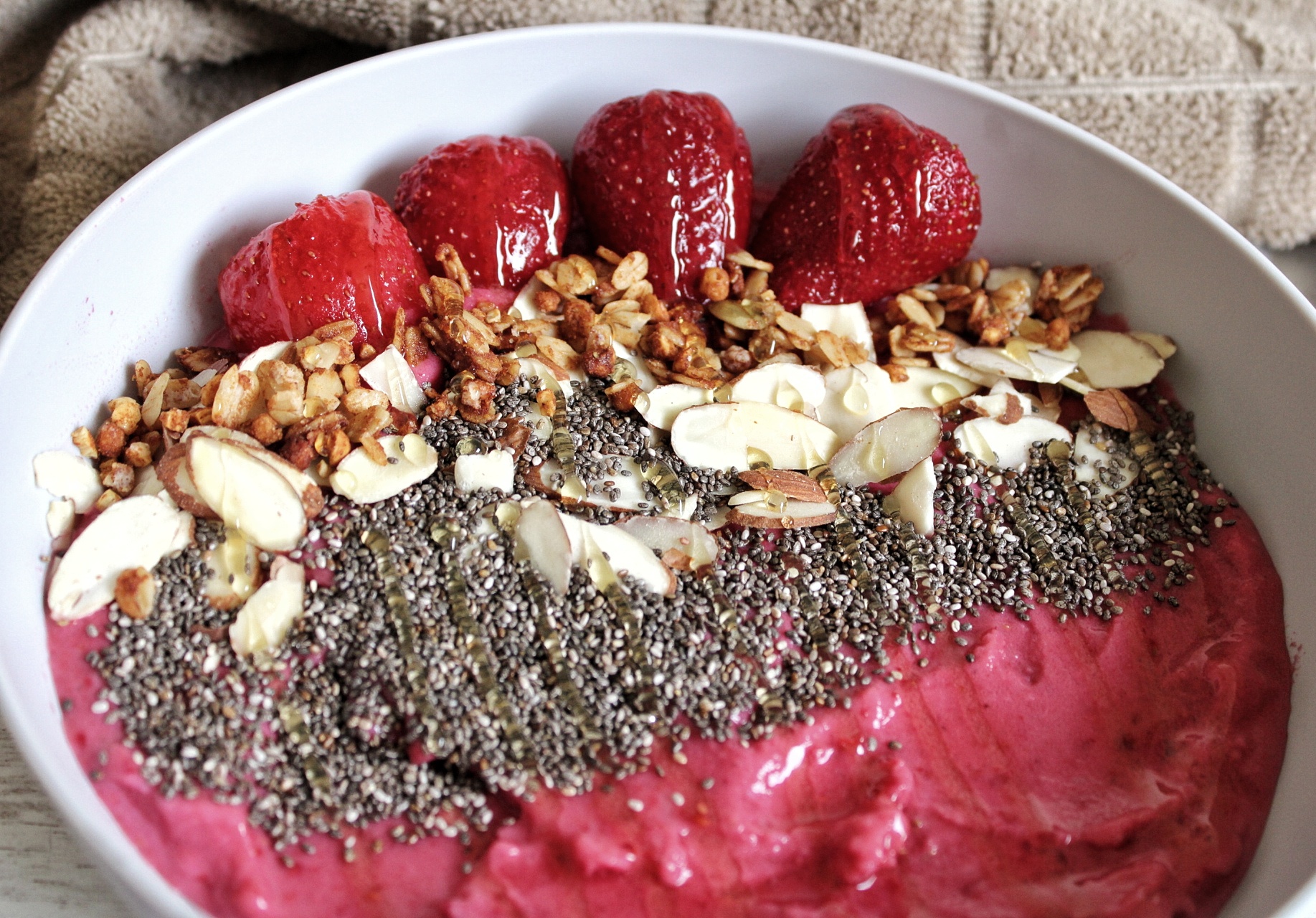 Strawberry raspberry smoothie bowl topped with chia seeds, nuts, granola, and honey.