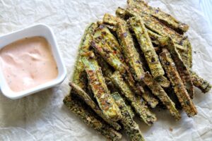 Baked zuchini fries on parchment paper with a side of dipping sauce