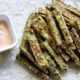 Baked zuchini fries on parchment paper with a side of dipping sauce