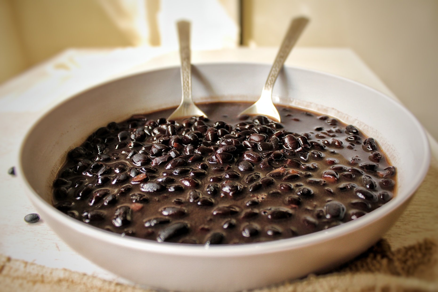 A bowl of cooked, saucy black beans on a table 