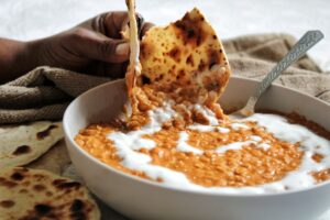 Dipping naan in a bowl of peanut butter red lentil curry