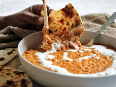 Dipping naan in a bowl of peanut butter red lentil curry