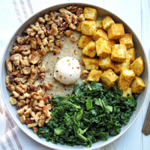 Oat bran in a gray bowl topped with walnuts, kale, tofu, vegan butter, and red chili pepper