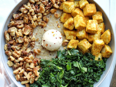 Oat bran in a gray bowl topped with walnuts, kale, tofu, vegan butter, and red chili pepper