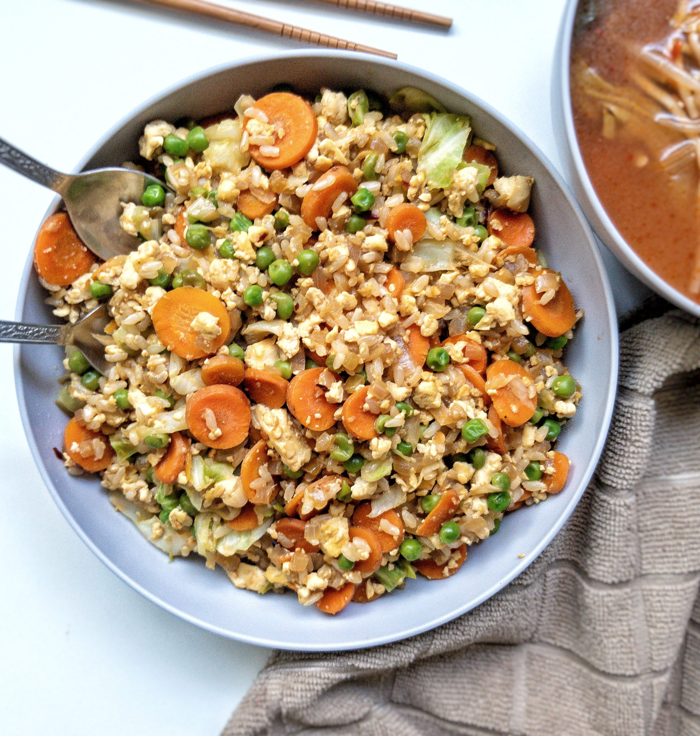 Vegan fried rice with carrots, peas, cabbage, and tofu scramble in a gray bowl 