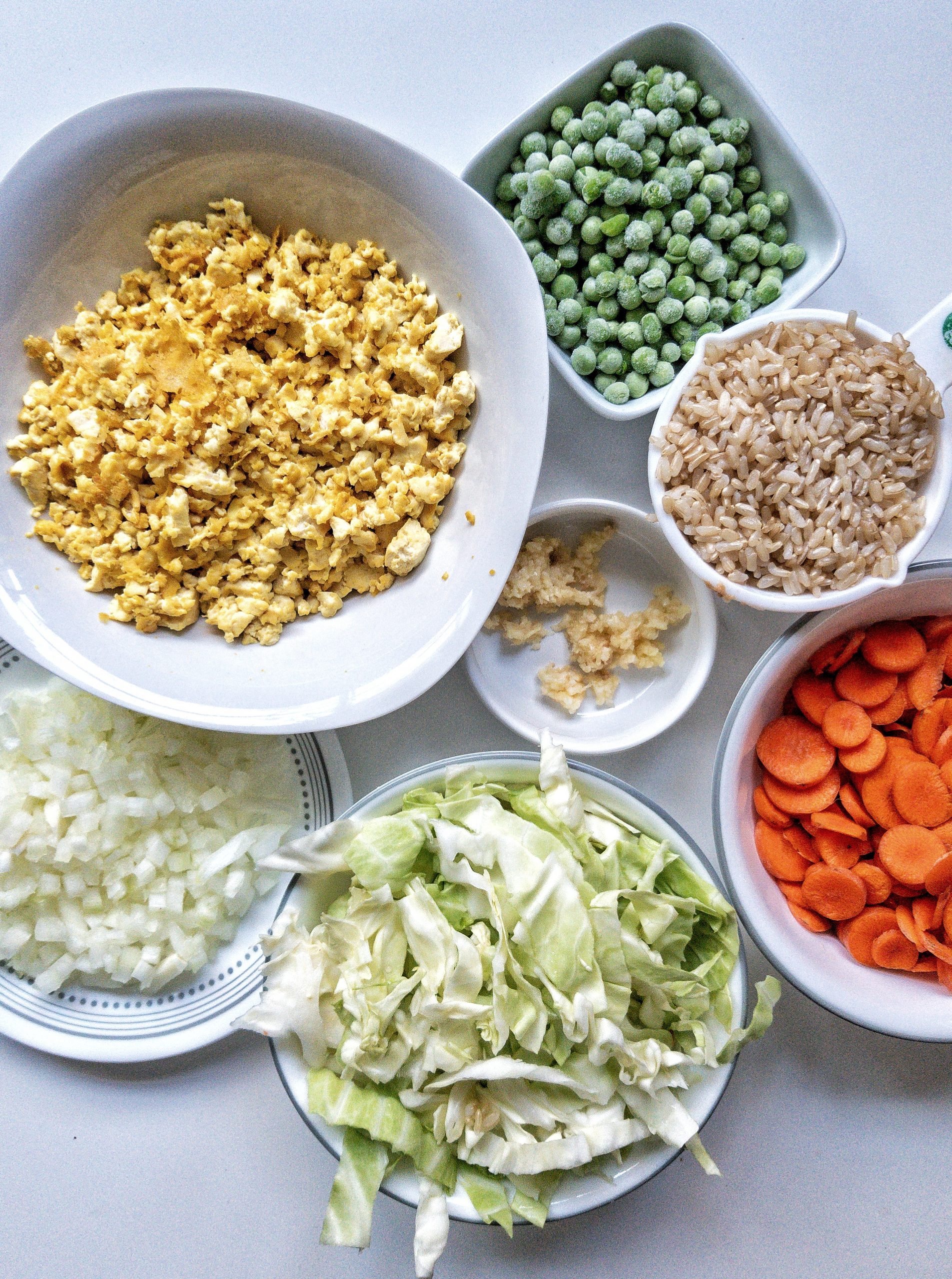 Oil-free, vegan fried rice ingredients including tofu scramble, chopped onion, cabbage, carrots, crushed garlic, frozen peas, and cooked brown rice 