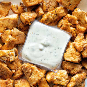 Vegan tofu "chicken" chunks on a platter with a white dipping sauce in the middle.