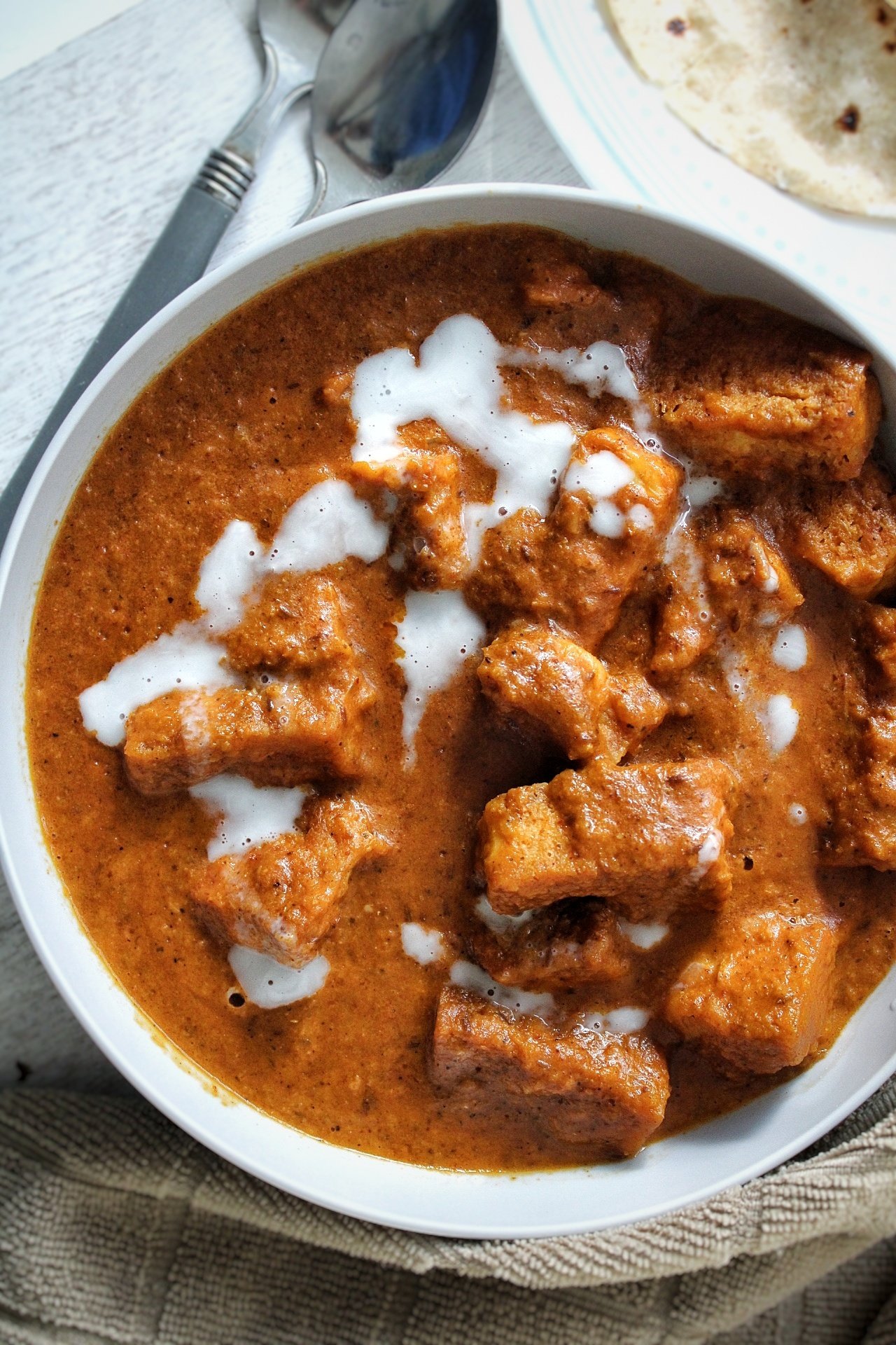 Bowl of vegan, tofu butter chicken topped with cream in a gray bowl