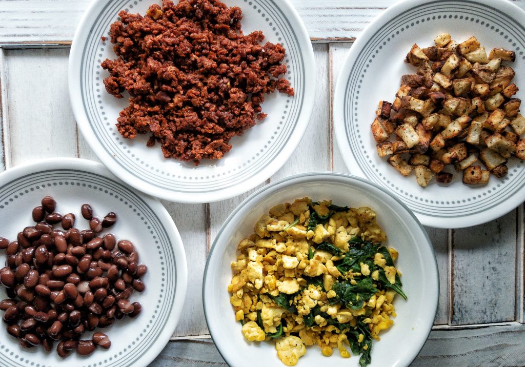 White plates with cooked soyrizo, potatoes, beans, and tofu scramble with greens 