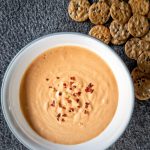 Cashew-based cheese sauce in a white bowl topped with a side of crackers