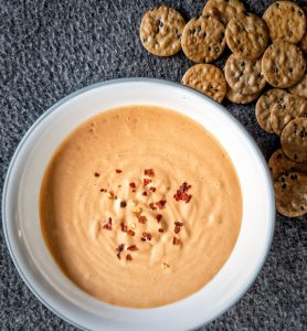 Cashew-based cheese sauce in a white bowl topped with a side of crackers