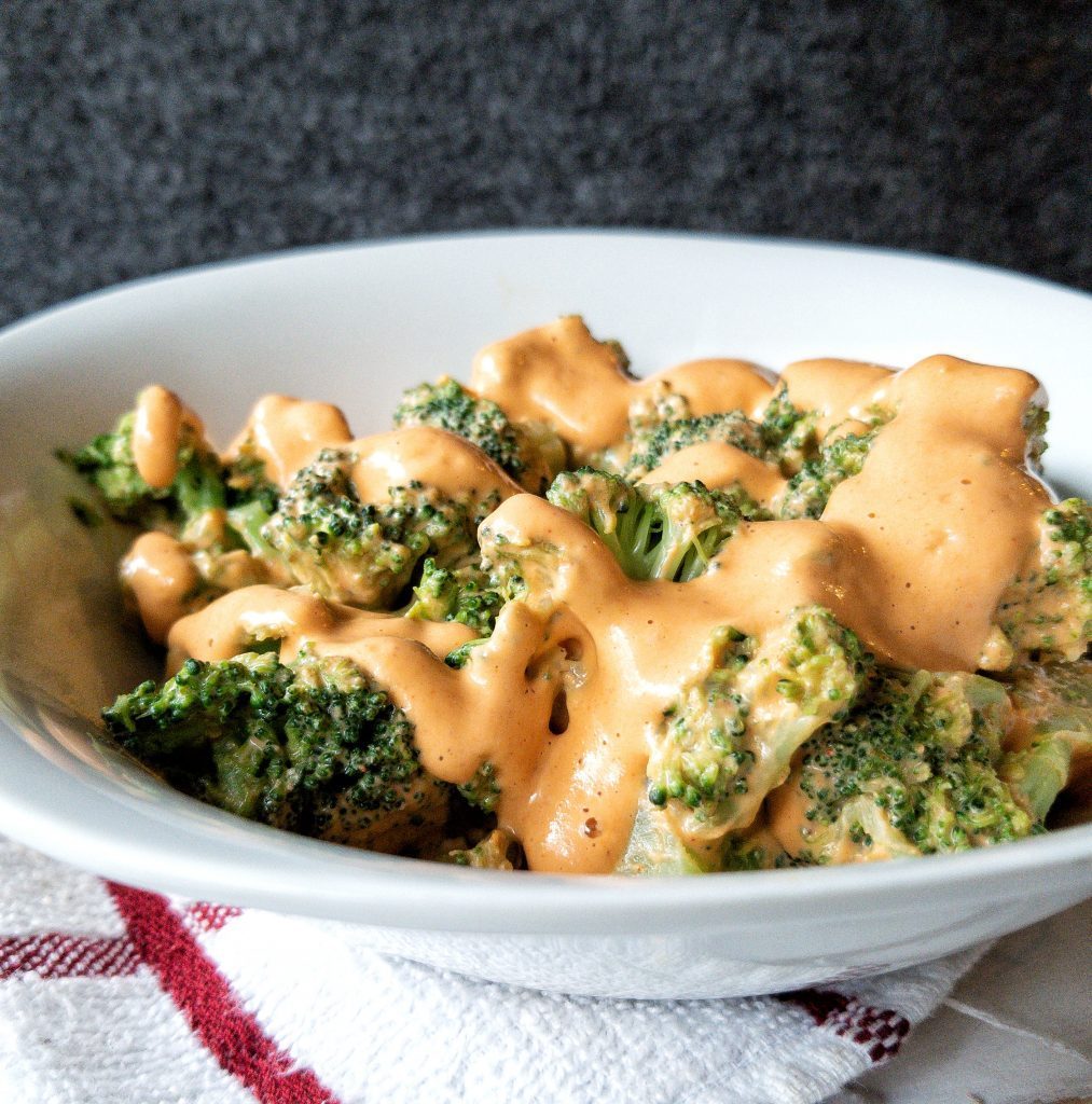 Roasted broccoli in a bowl with homemade, vegan cheese sauce on top