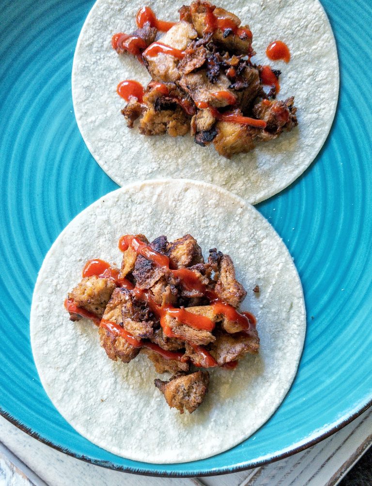 Soft tacos topped with tofu vegan chicken and a hot sauce