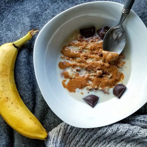 White bowl with oat bran topped with peanut butter and chocolate chunks