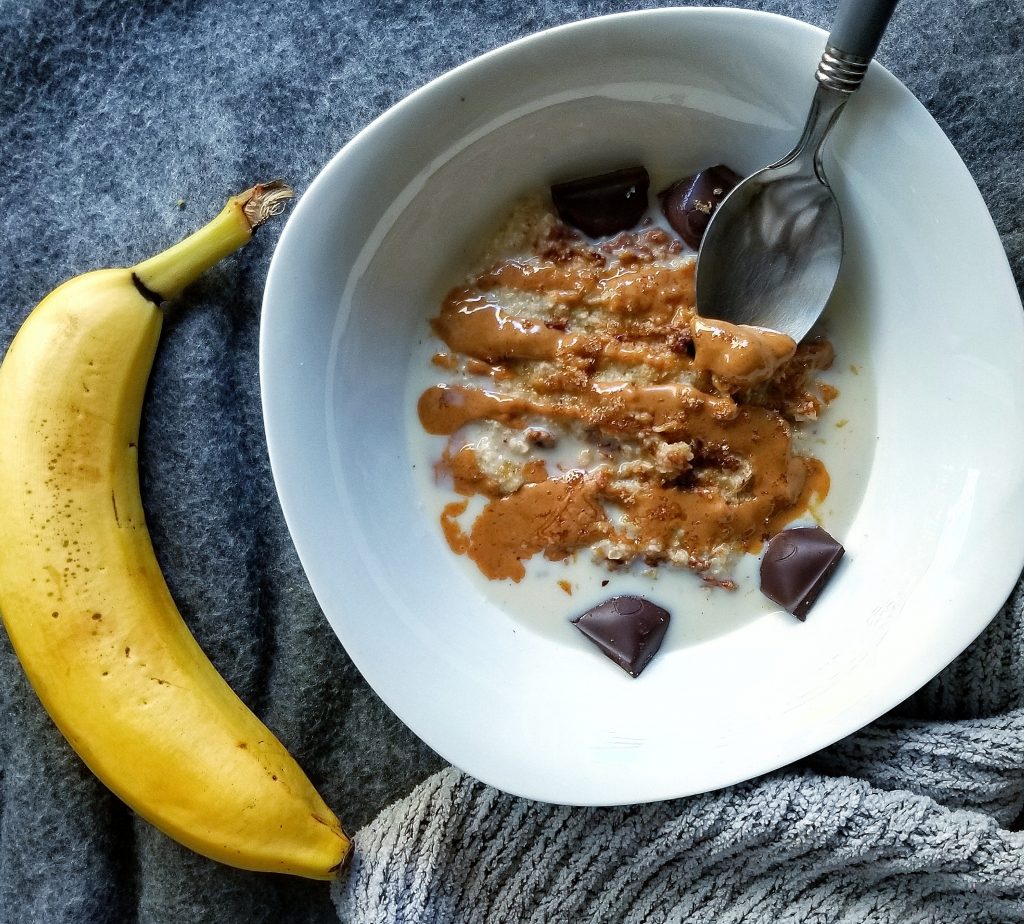 White bowl with oat bran topped with peanut butter and chocolate chunks