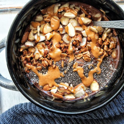 A chocolate banana smoothie bowl topped with peanut butter, chia seeds, sliced almonds, and granola