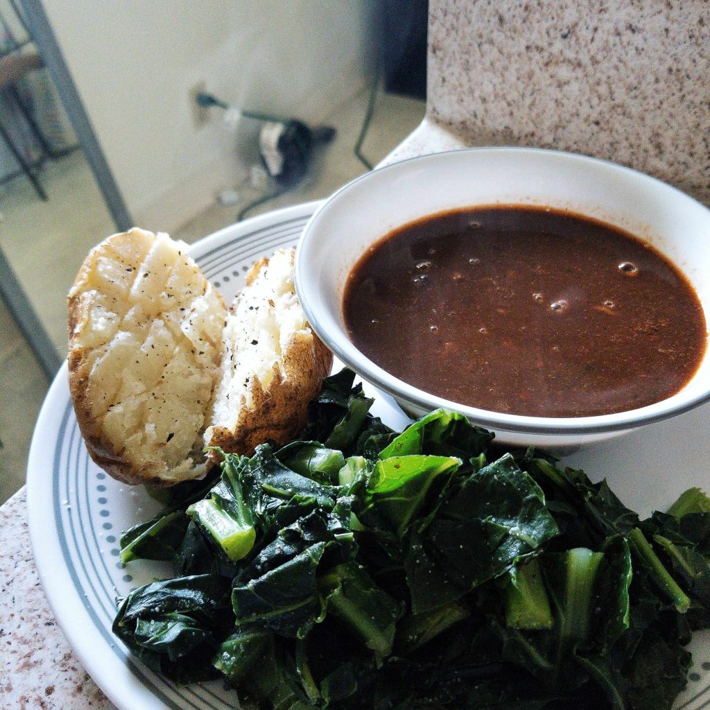 Plate with black bean soup, baked potato, and greens