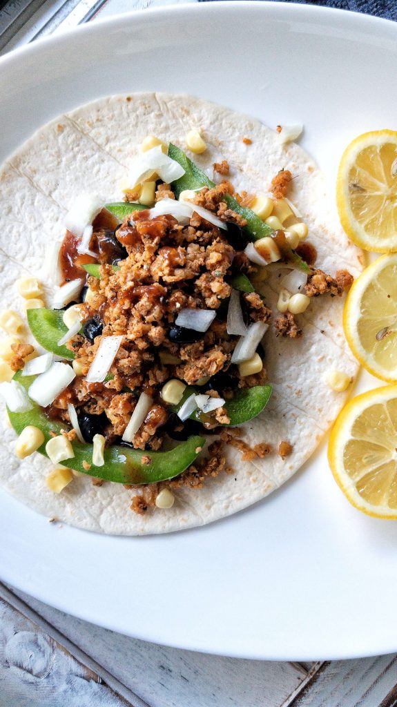 Flour tortilla topped with vegetables and walnut meat with a side of sliced lemon