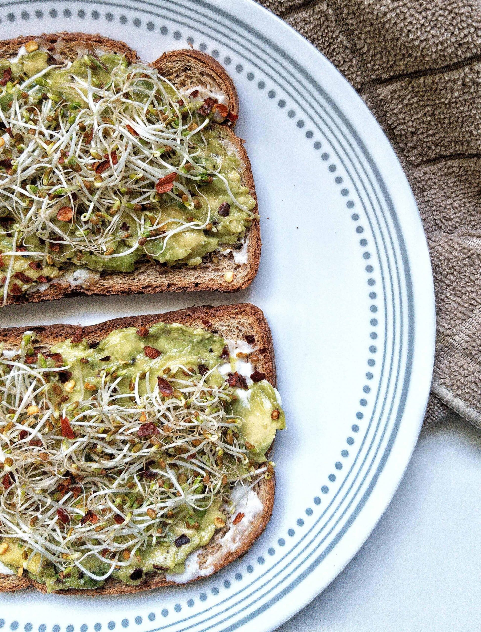 Avocado toast on whole wheat bread topped with sprouts and a pinch of red chili flakes