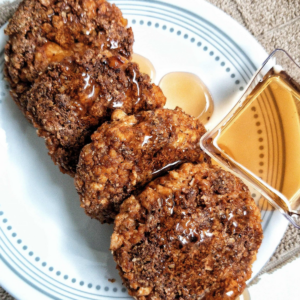 Round, flat sausage patties made with tofu. Topped with maple syrup with a small container on the side with more syrup.