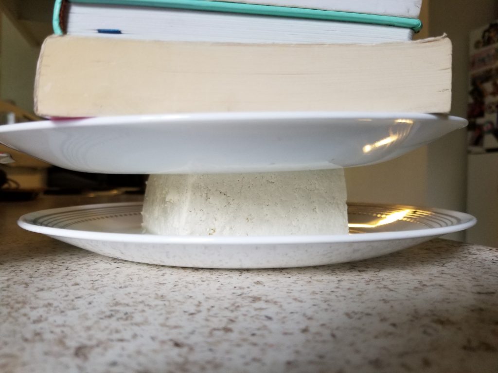 A plate on top of a block of tofu with books stacked on top to press excess water