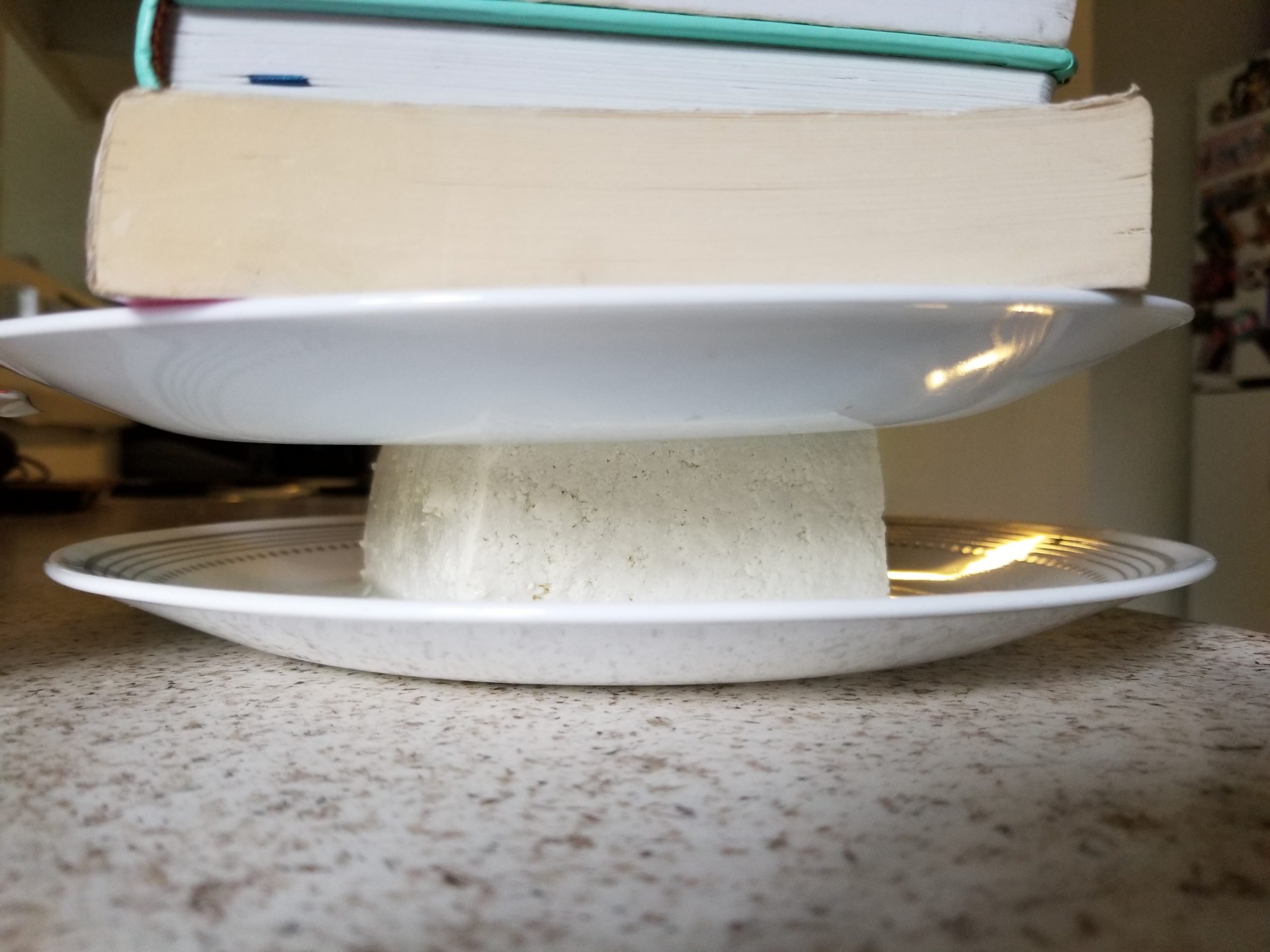 A plate on top of a block of tofu with books stacked on top to press excess water