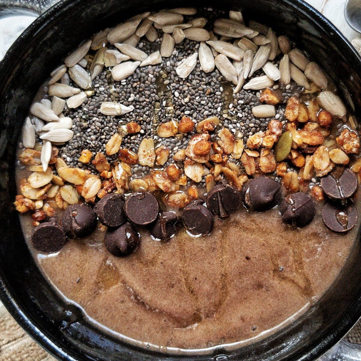 Coffee banana smoothie bowl topped with chia seeds, sunflower seeds, granola, chocolate chips, drizzle of honey