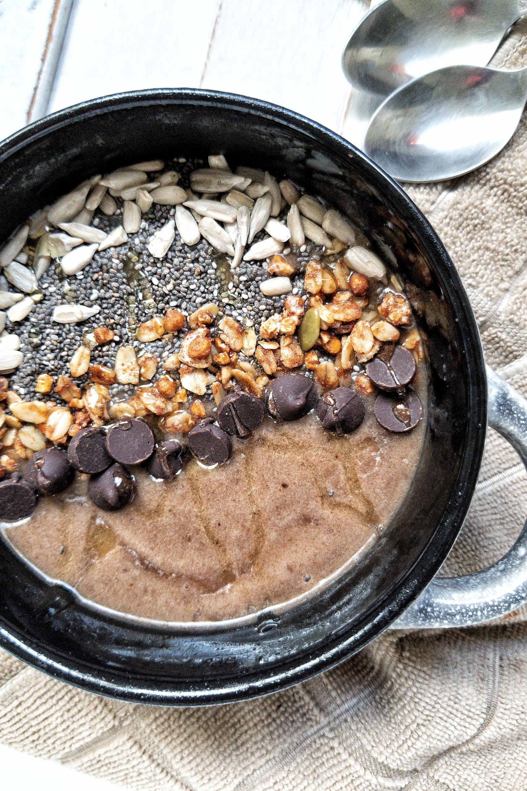 A coffee smoothie bowl topped with raw sunflower seeds, chia seeds, ganola, chocolate chip, and a drizzle of honey