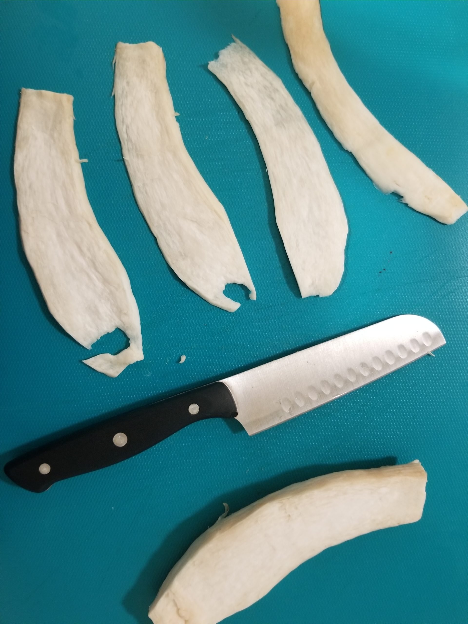 Thinly sliced king oyster mushrooms on a chopping board with a knife. 