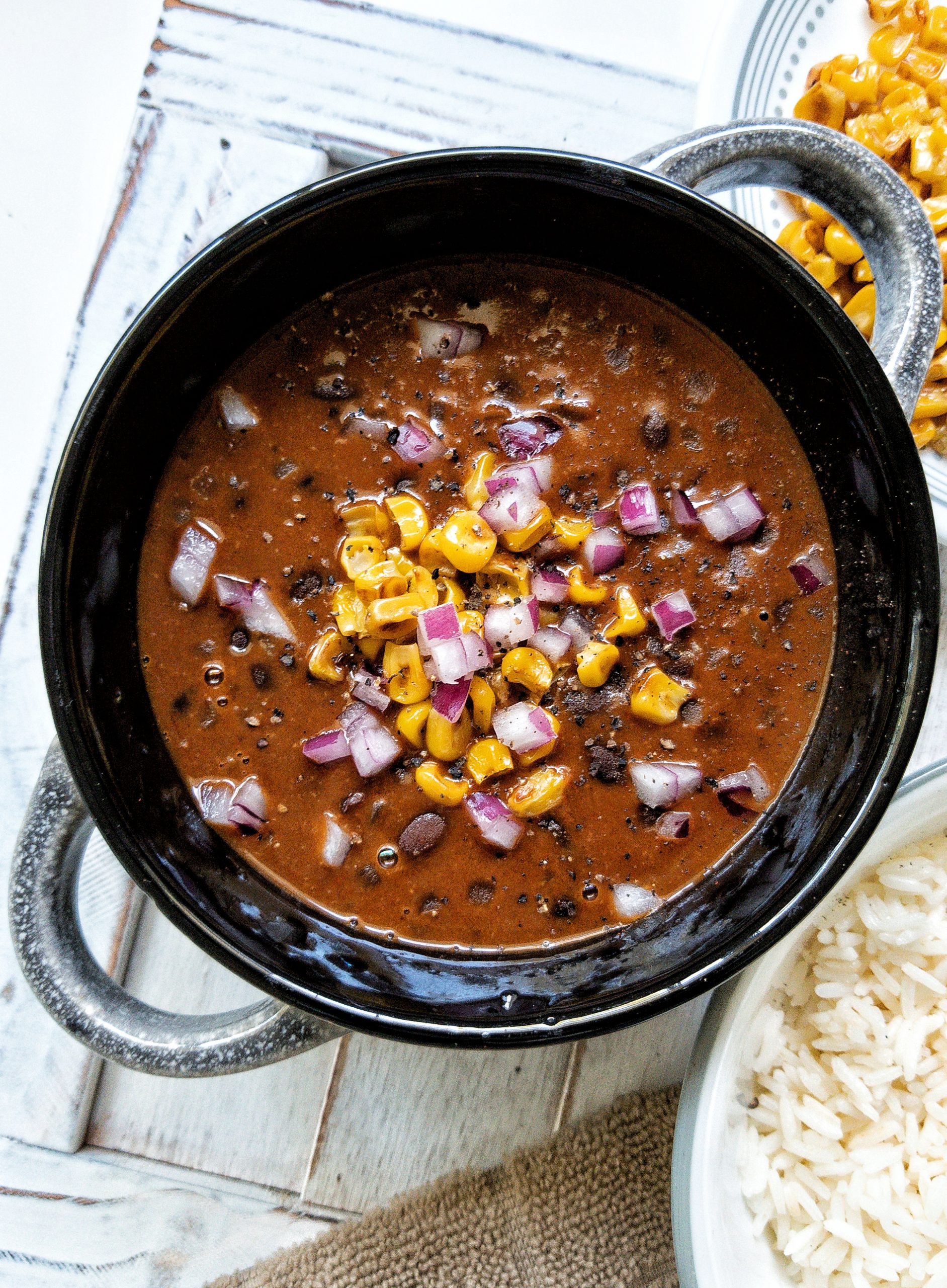 Black bean soup in a black bowl topped with pan-roasted corn, chopped red onions, and cracked black pepper