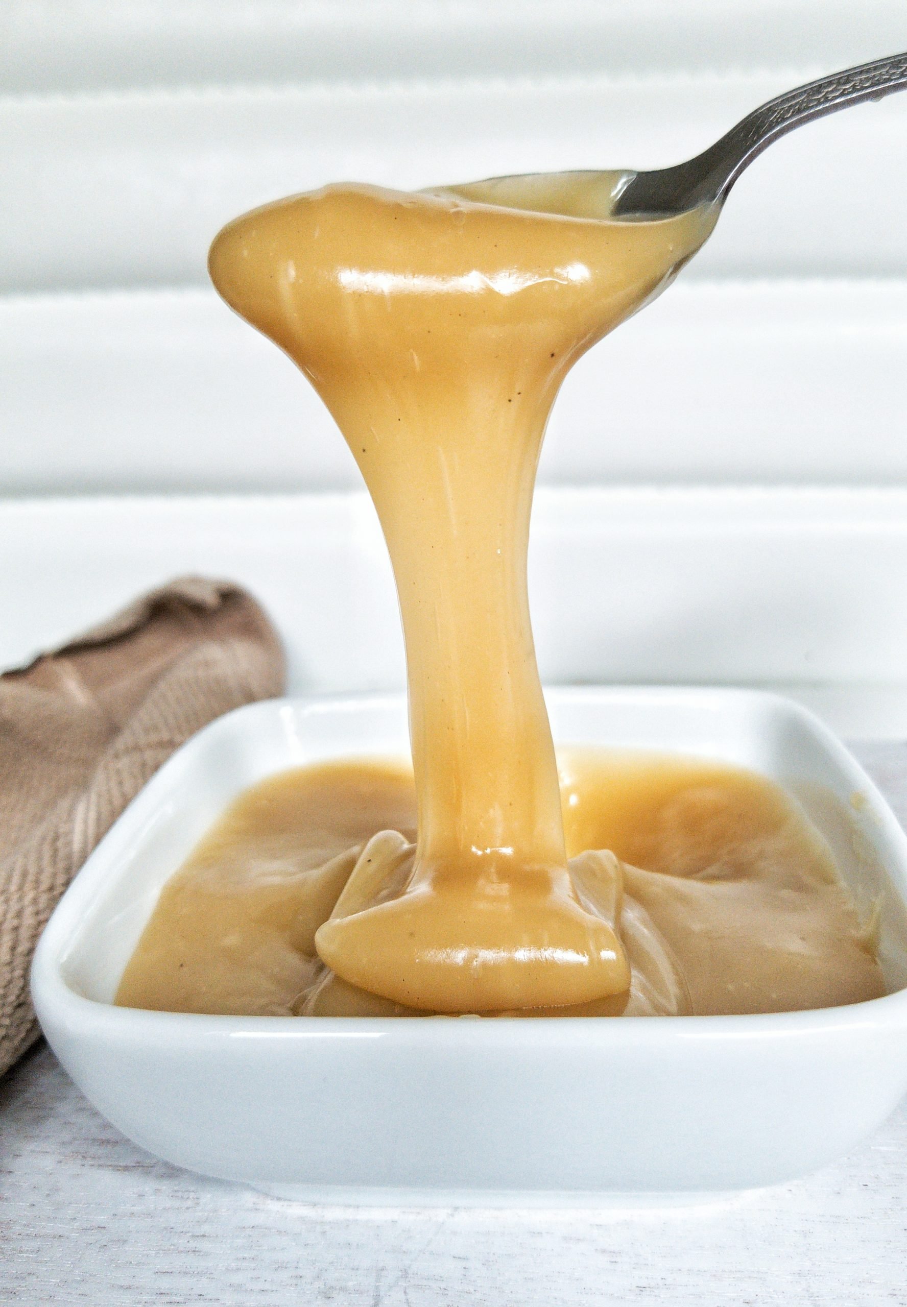 A spoon pouring coconut dulce de leche in to a small, white glass dish