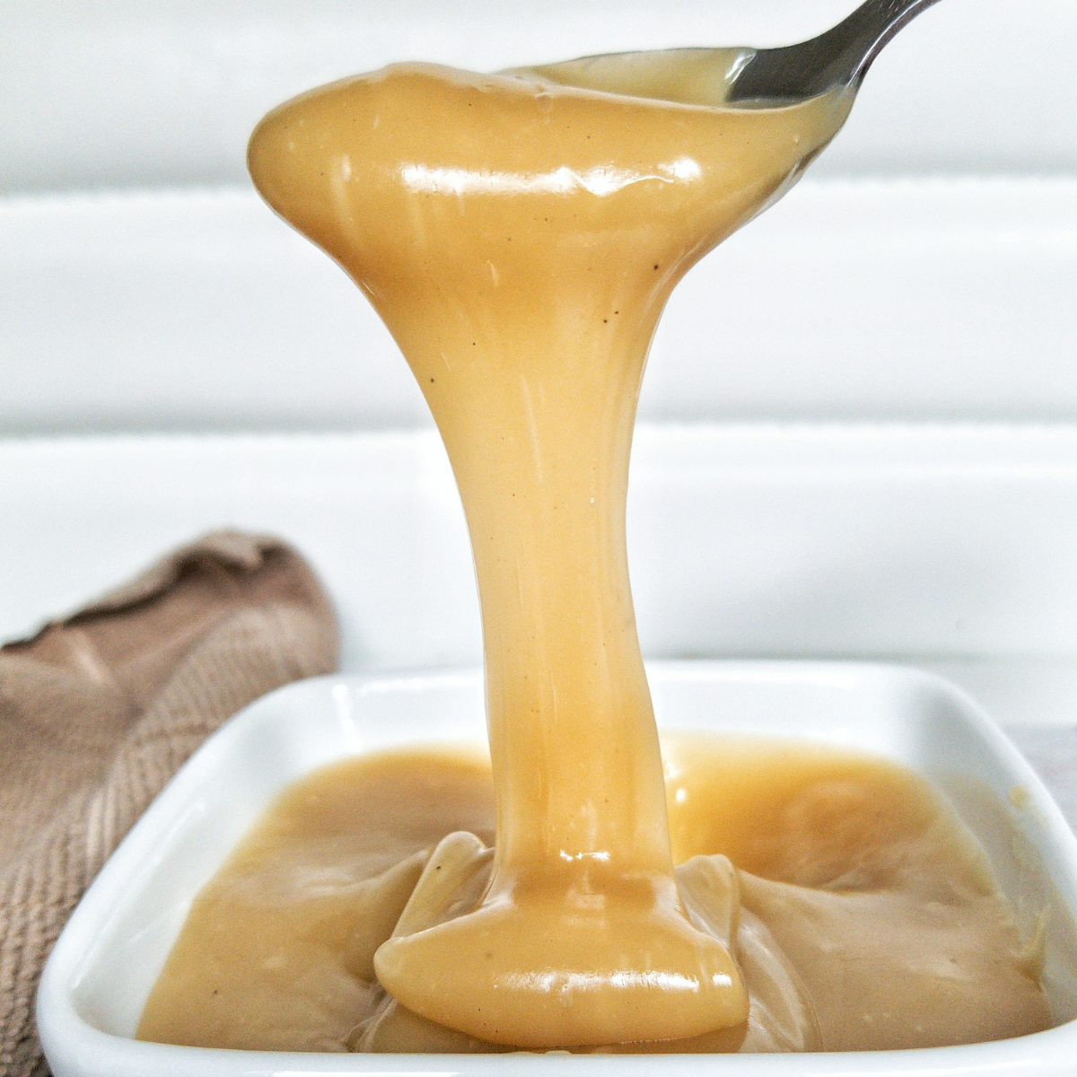 dairy-free dulce de leche in a white bowl, stretched with a spoon