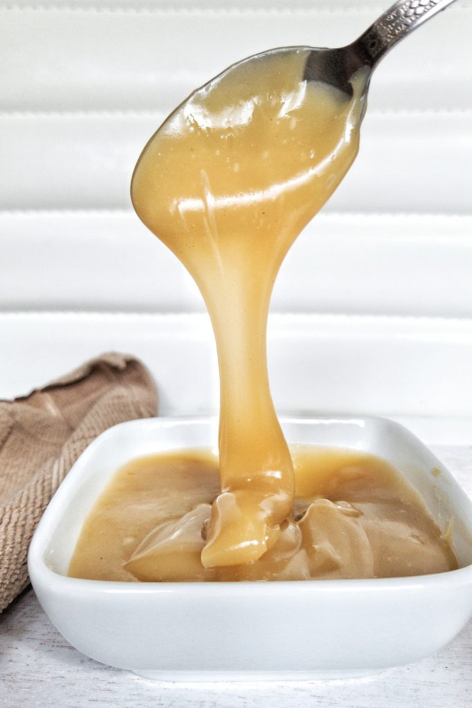 Close-up of dulce de leche being poured into a small, white, glass dish.