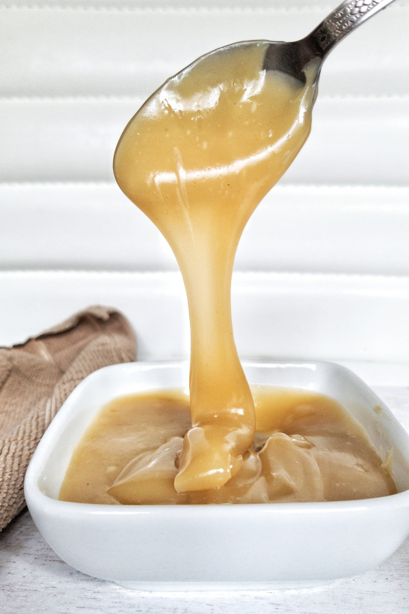 Close-up of dulce de leche being poured into a small, white, glass dish. 