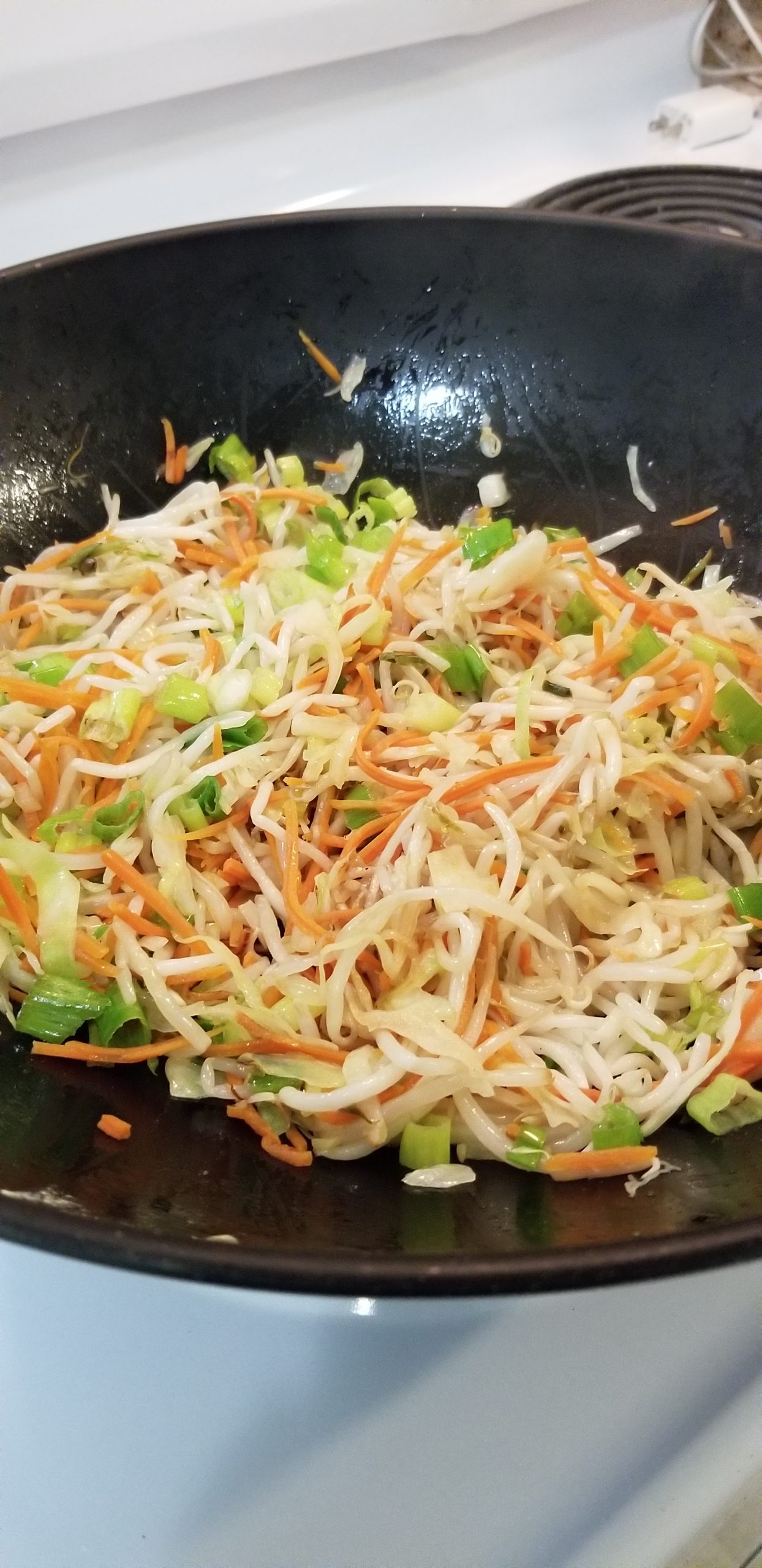 Mung bean sprouts, shredded carrots, shredded cabbage, and green onions cooking in a wok