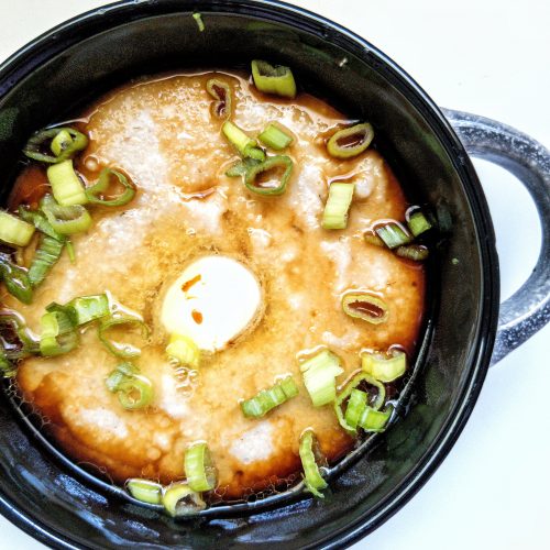 Bowl of cooked oat bran topped with chopped green onions, vegan butter, and soy sauce