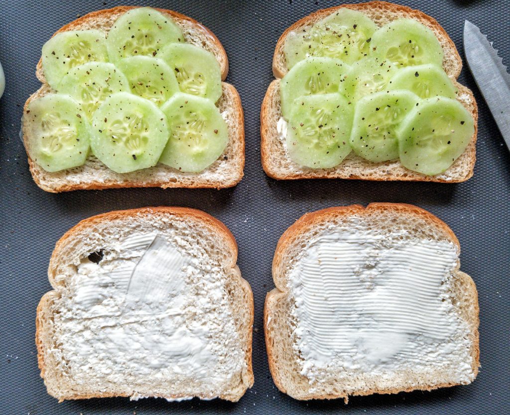 Four slices of buttered, white bread. Two slices with sliced cucumber, salt, and ground black pepper