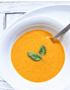 Blended and smooth roasted tomato basil soup in a white bowl garnished with two basil leaves