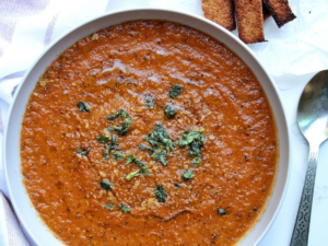 Vegan roasted tomato basil soup topped with chopped basil and a side of toasted bread.