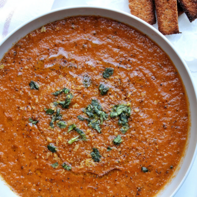 Vegan roasted tomato basil soup topped with chopped basil and a side of toasted bread.