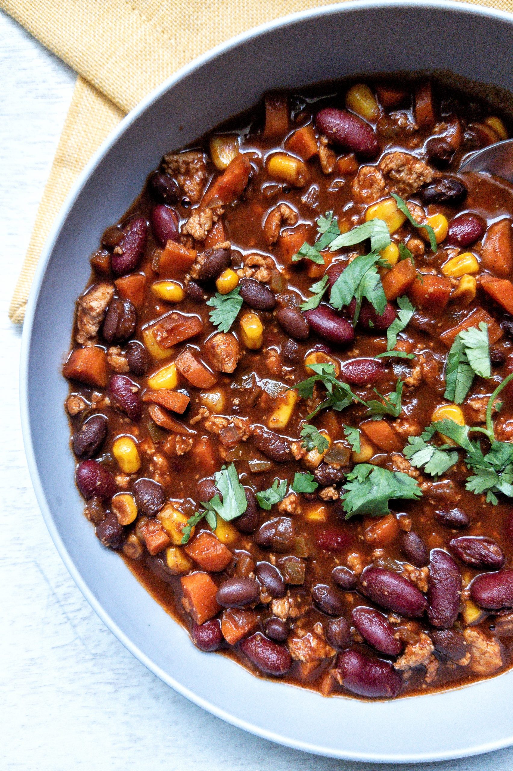 Tofu bean chili in a large, gray bowl with a yellow napkin. Served with chopped cilantro on top