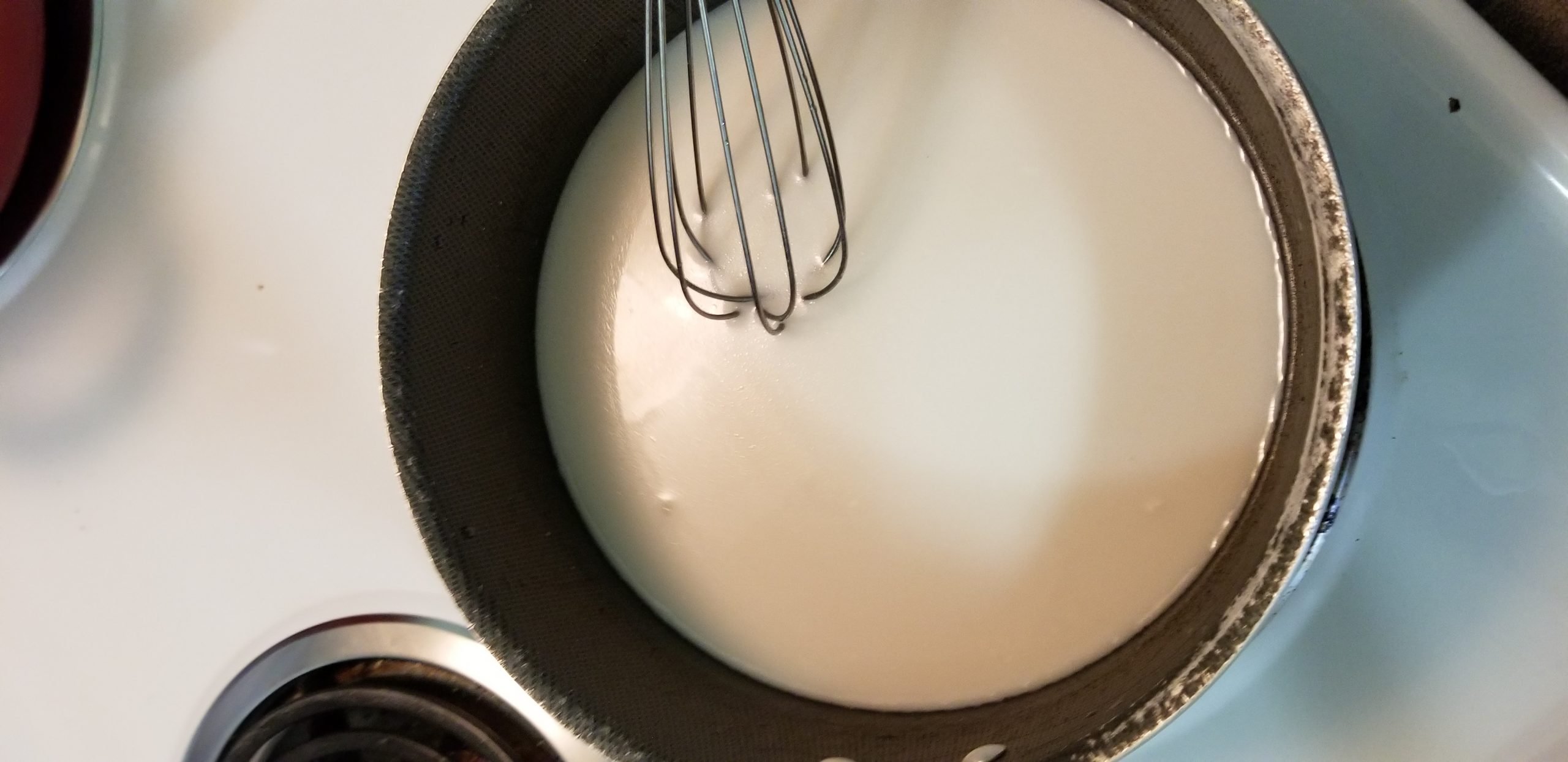 Saucepan with coconut milk and sugar and a whisk