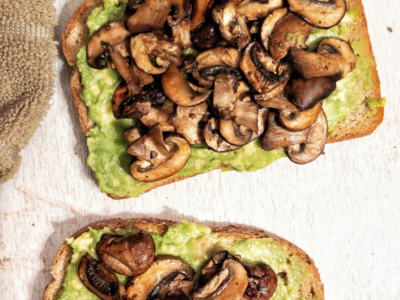 Sliced brown mushrooms on two slices of avocado toast