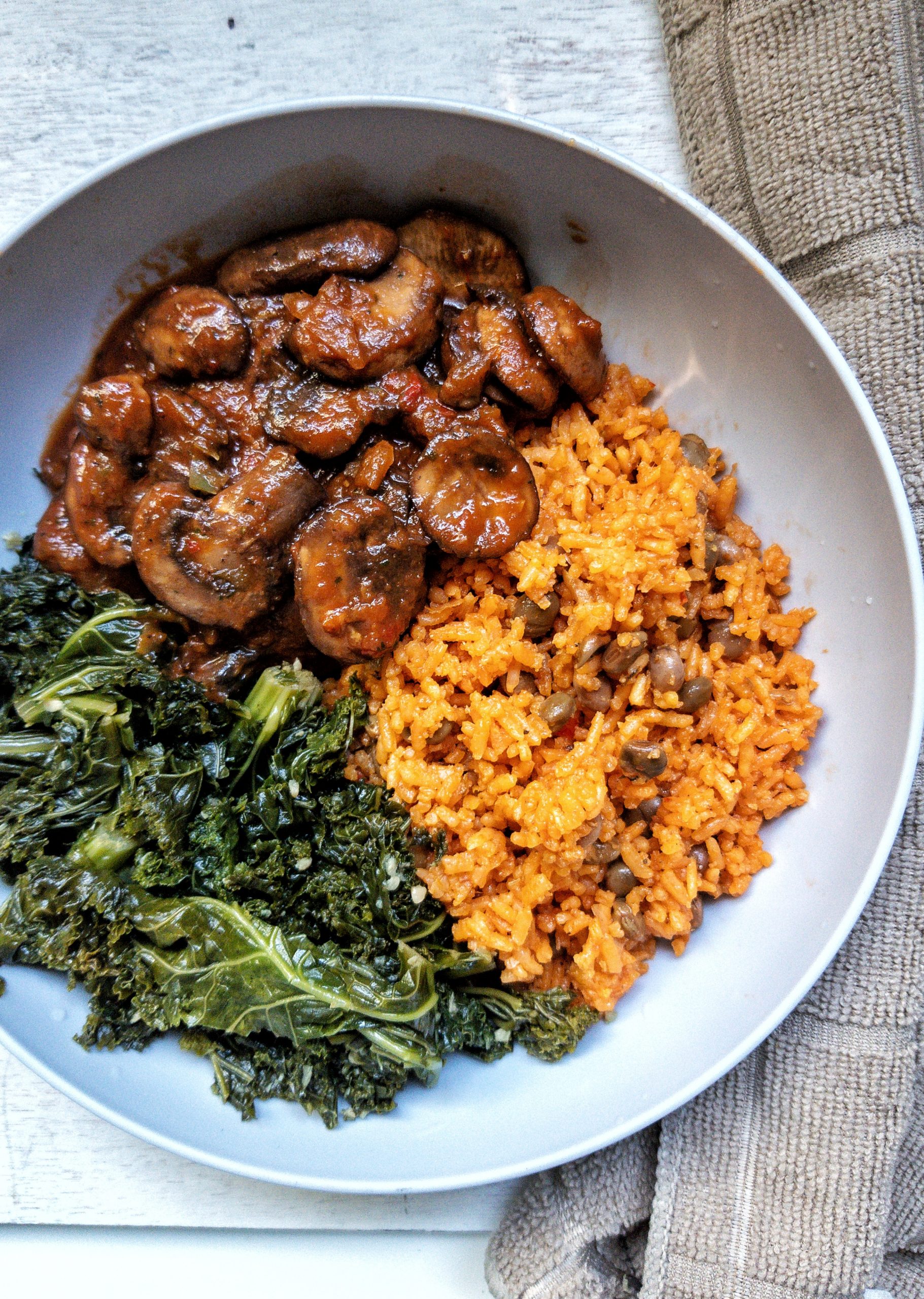 Puerto Rican yellow rice with a side of stewed mushrooms and braised kale in a gray bowl