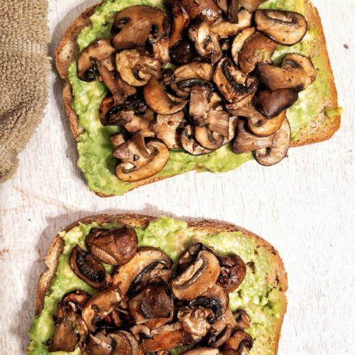 Two slices of toasted bread topped with smashed avocado and mushrooms