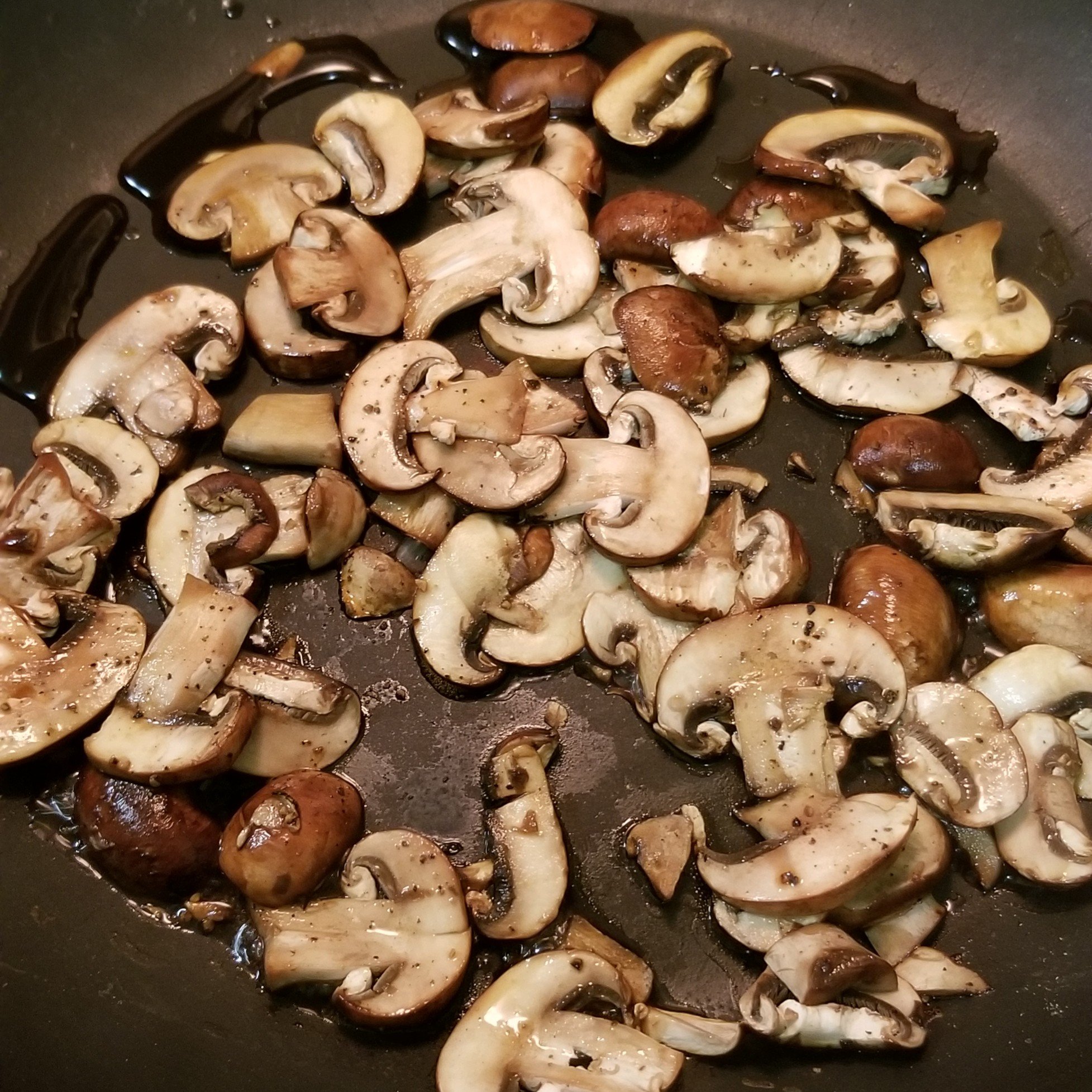 Sliced common mushrooms cooking in a non-stick pan with low-sodium soy sauce