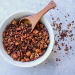 Vegan sausage crumbles in a white bowl with a wooden spoon.